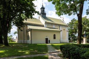 widok na odnowiony kościół z zewnątrz otoczony zielenią pobliskich drzew, słoneczny dzień,