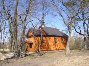 widok na drewniany kościół, obok rosnące drzewa, słoneczny dzień w porze jesienno-zimowej