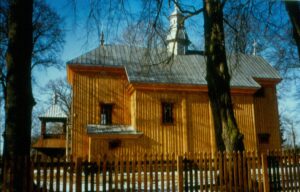widoczny drewniany kościół obok drewniana dzwonnica i płot