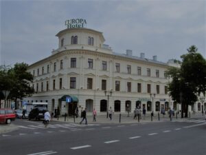 widok na hotel z zewnątrz, letnia pora, obok chodnikiem spacerują ludzie