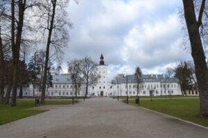 widok na założenie zespołu zamkowego, na pierwszym planie widać fragment parku z uliczkami i przystrzyżoną trawą w tle widoczne budynki w kolorze bieli.