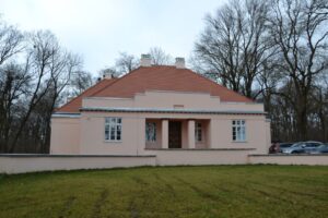 widok na różowy budynek dworu widoczny trawnik i otaczające dwór drzewa